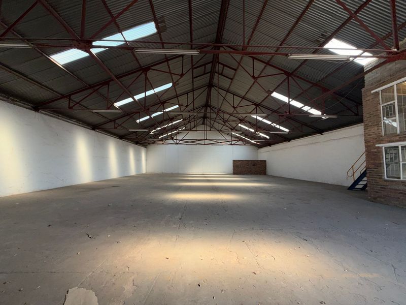 Spacious industrial warehouse featuring high ceilings with exposed steel trusses, natural light from skylights, and durable concrete flooring.