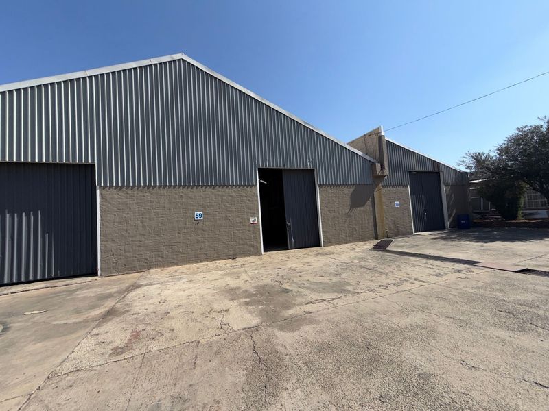 Exterior view of industrial warehouse units featuring corrugated metal cladding, sliding access doors, and a concrete yard area.