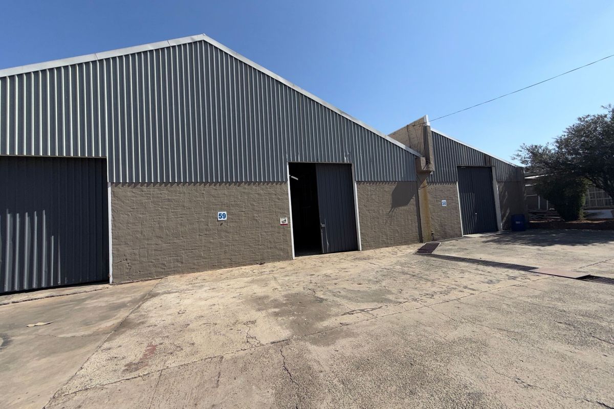 Exterior view of industrial warehouse units featuring corrugated metal cladding, sliding access doors, and a concrete yard area.