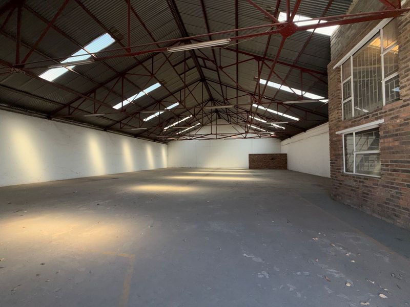 Spacious industrial warehouse unit featuring high exposed steel roof trusses, concrete flooring, and natural light through integrated skylights.