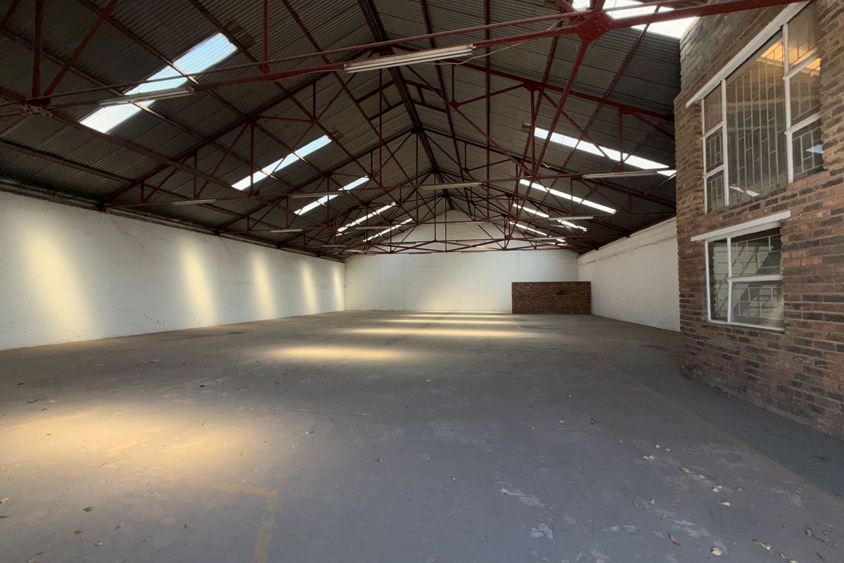 Spacious industrial warehouse unit featuring high exposed steel roof trusses, concrete flooring, and natural light through integrated skylights.