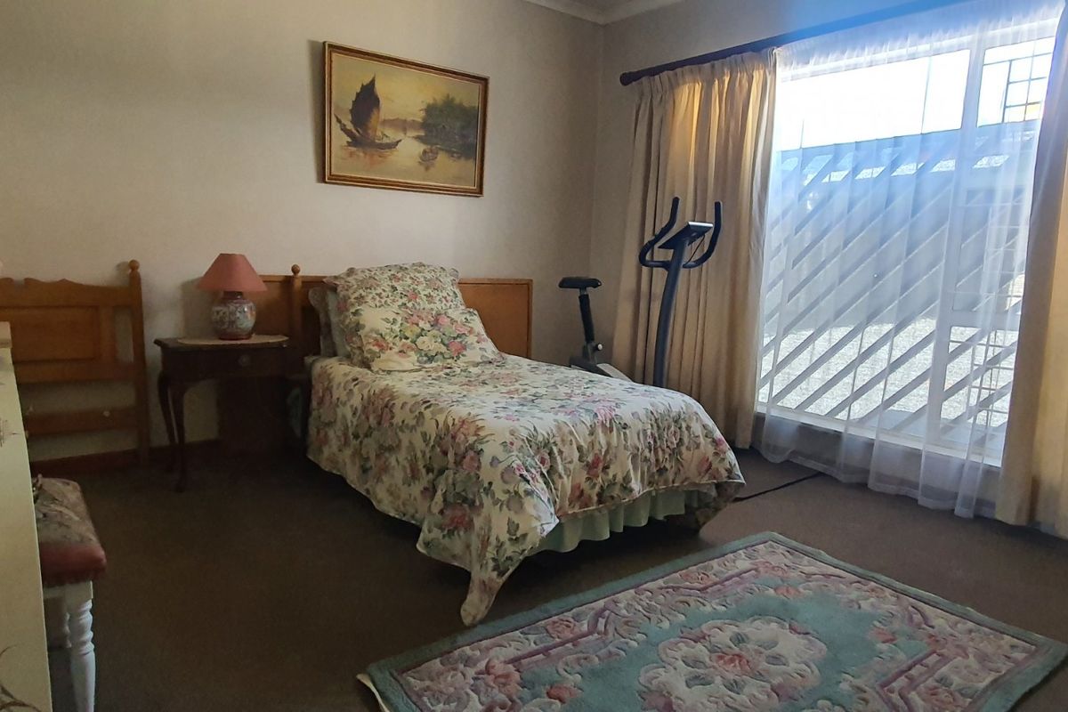 A carpeted bedroom featuring a large window with security bars and a built-in headboard, offering a functional and well-lit living space.