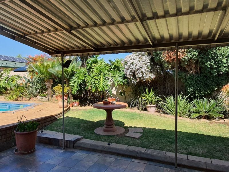 A covered patio area overlooking a private swimming pool and a well-established garden with mature landscaping.
