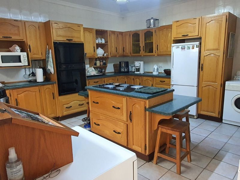 A spacious kitchen featuring extensive wooden cabinetry, a central island with a cooktop, and tiled finishes throughout.