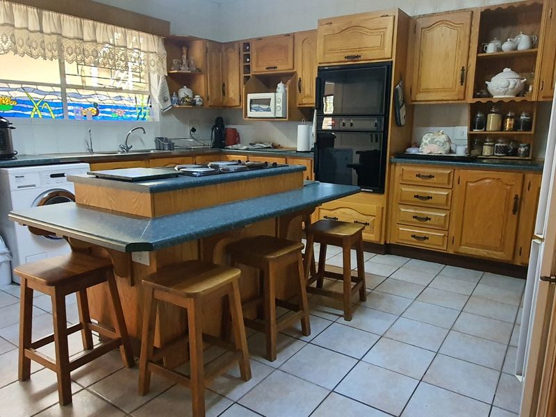 A spacious kitchen featuring extensive wooden cabinetry, a central island with seating, built-in oven, and a decorative stained glass window above the sink area.