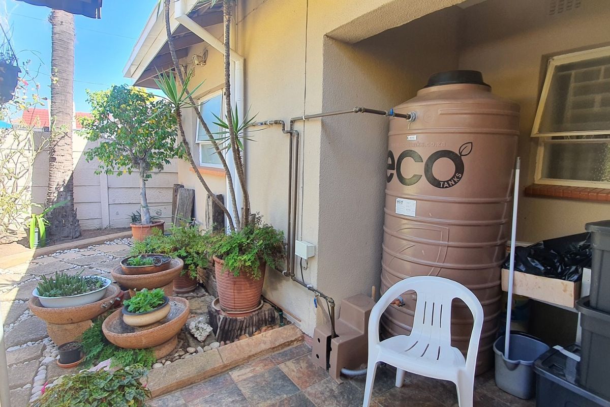 Rear exterior area featuring a large water storage tank, external plumbing, and a paved patio surface.