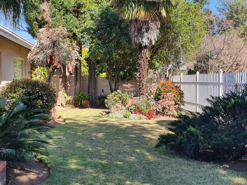 A well-maintained private garden featuring mature trees, established landscaping, and a white picket fence boundary.