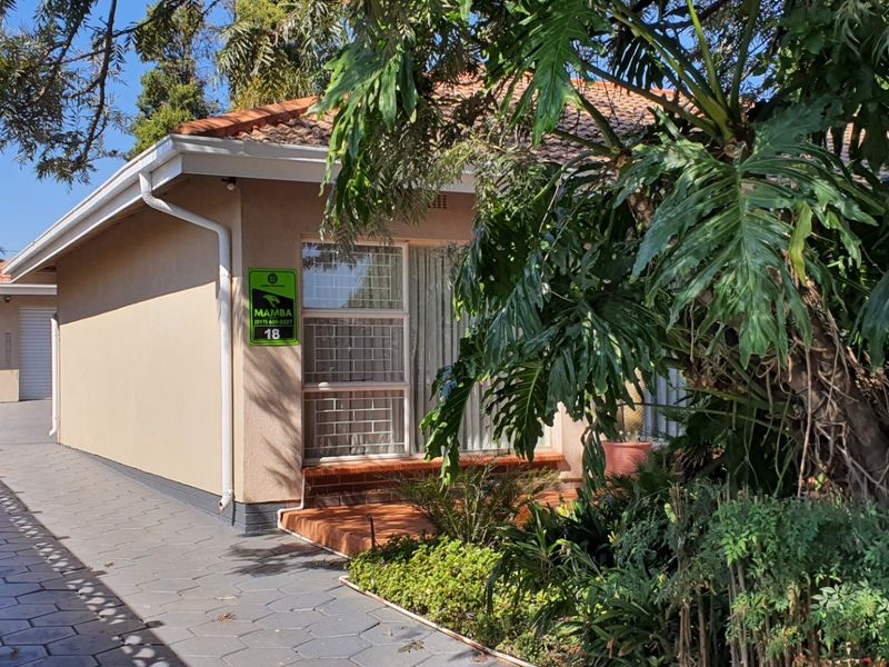 Front elevation of a single-story residence featuring a paved driveway, carport, and established garden surroundings.