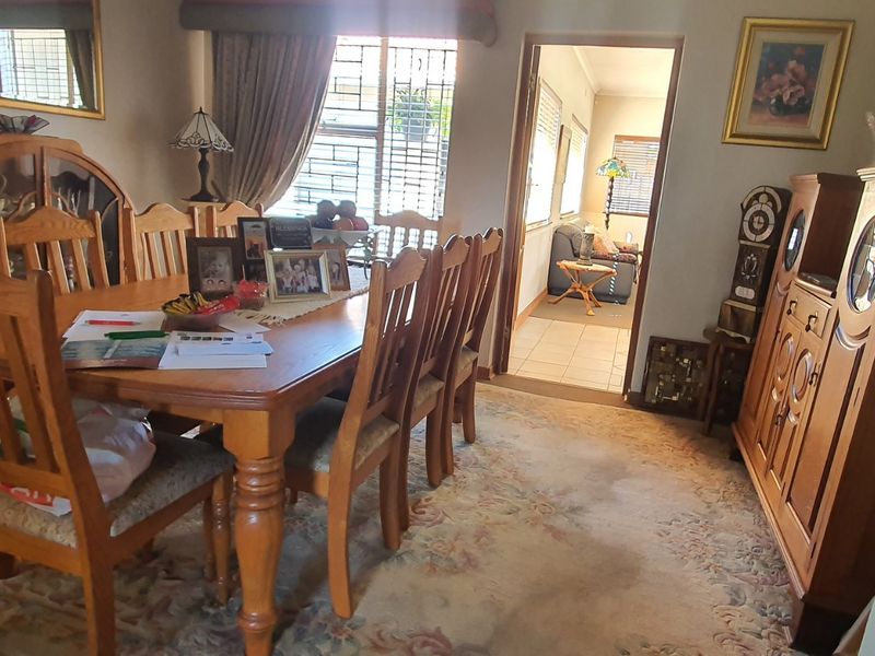 A traditional dining room featuring carpeted flooring and security bars on the windows, with an open doorway leading to an adjacent living area.