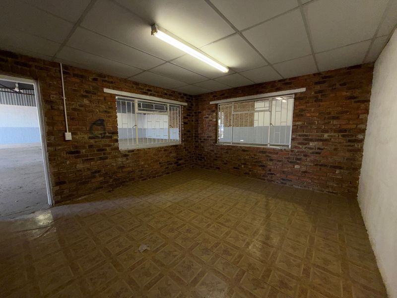 An empty industrial office space featuring exposed brick walls, tiled flooring, and a suspended ceiling with fluorescent lighting.