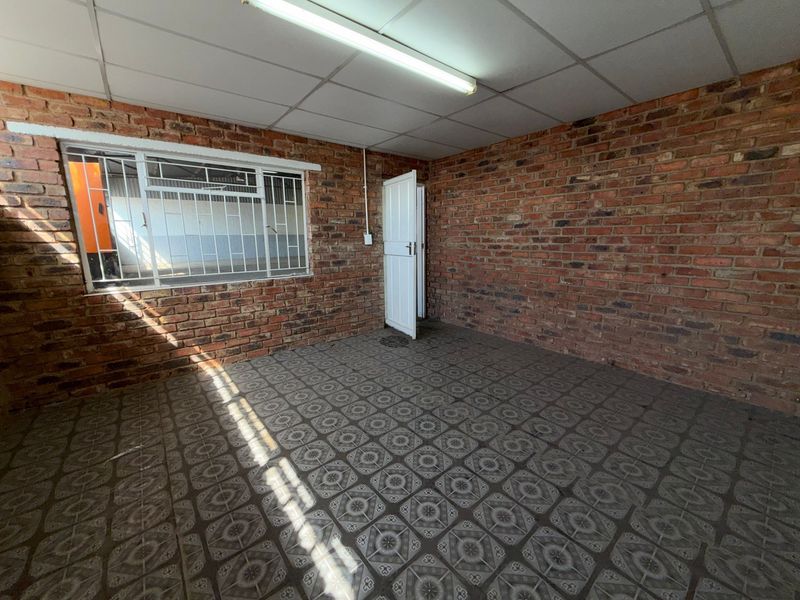 An empty industrial-style office space featuring exposed brick walls, tiled flooring, and a drop ceiling with fluorescent lighting.