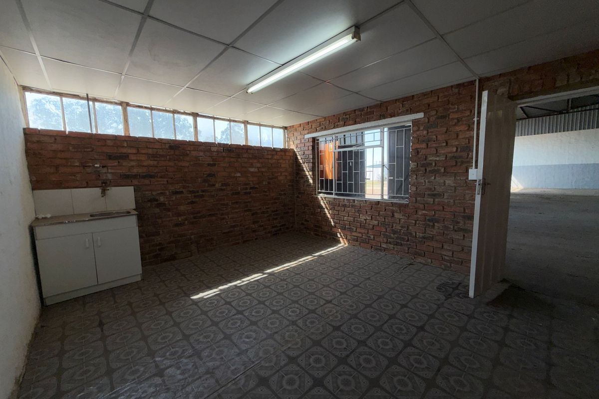 A functional industrial-style kitchenette featuring exposed brick walls, tiled flooring, and a basic built-in sink unit, offering a blank canvas for renovation.