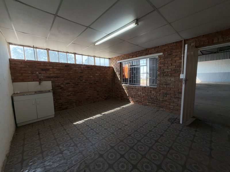 A functional industrial-style kitchenette featuring exposed brick walls, tiled flooring, and a basic built-in sink unit, offering a blank canvas for renovation.
