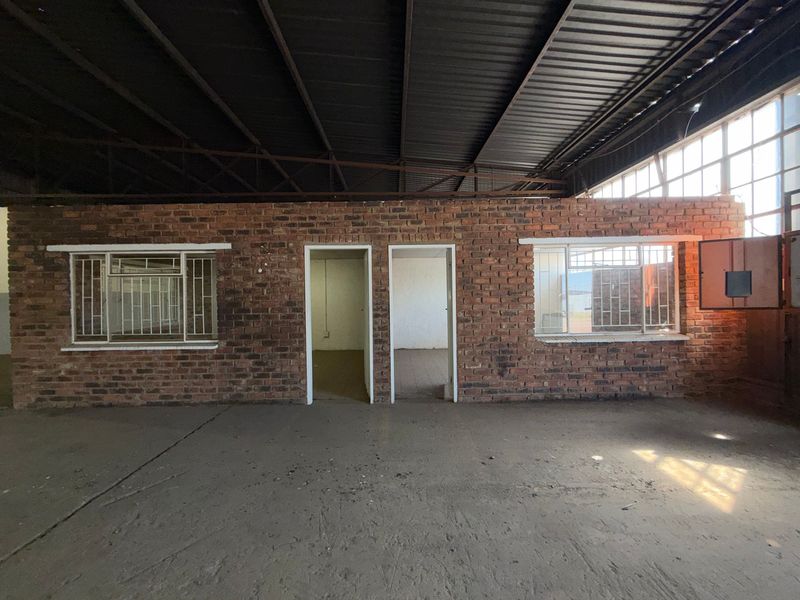 Industrial utility space featuring exposed brick partition walls, steel roof trusses, and concrete flooring, suitable for workshop or storage use.