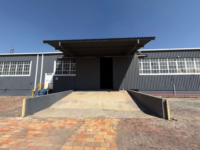 Industrial warehouse exterior featuring a large loading ramp, steel canopy, and corrugated metal cladding with multiple industrial-style windows.