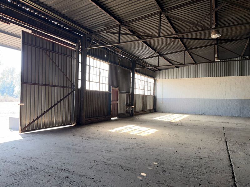 Spacious industrial warehouse unit featuring high ceilings with exposed steel trusses, concrete flooring, and large sliding access doors for versatile operational use.