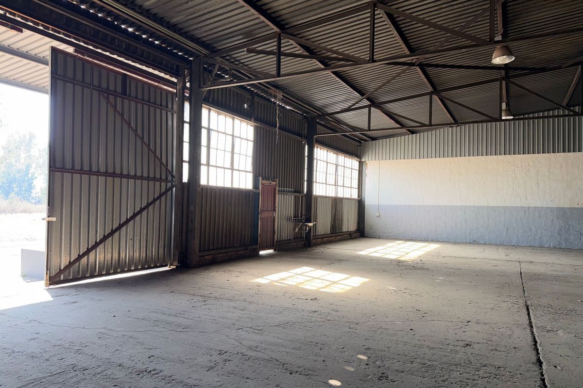 Spacious industrial warehouse unit featuring high ceilings with exposed steel trusses, concrete flooring, and large sliding access doors for versatile operational use.