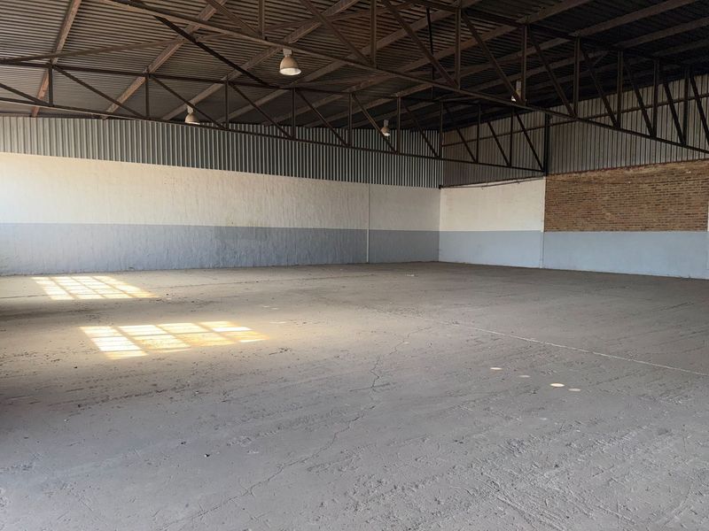 Spacious industrial warehouse unit featuring high exposed steel roof trusses, concrete flooring, and a combination of painted masonry and exposed brick walls.