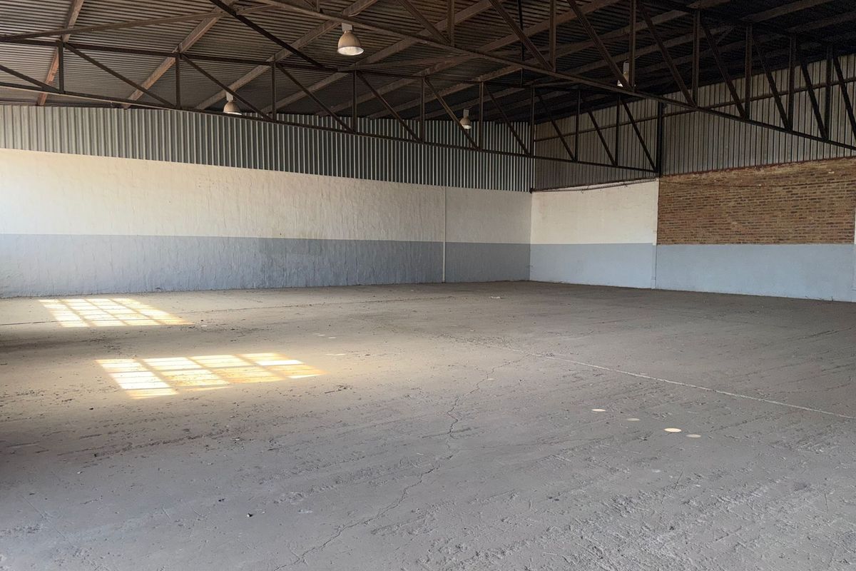 Spacious industrial warehouse unit featuring high exposed steel roof trusses, concrete flooring, and a combination of painted masonry and exposed brick walls.