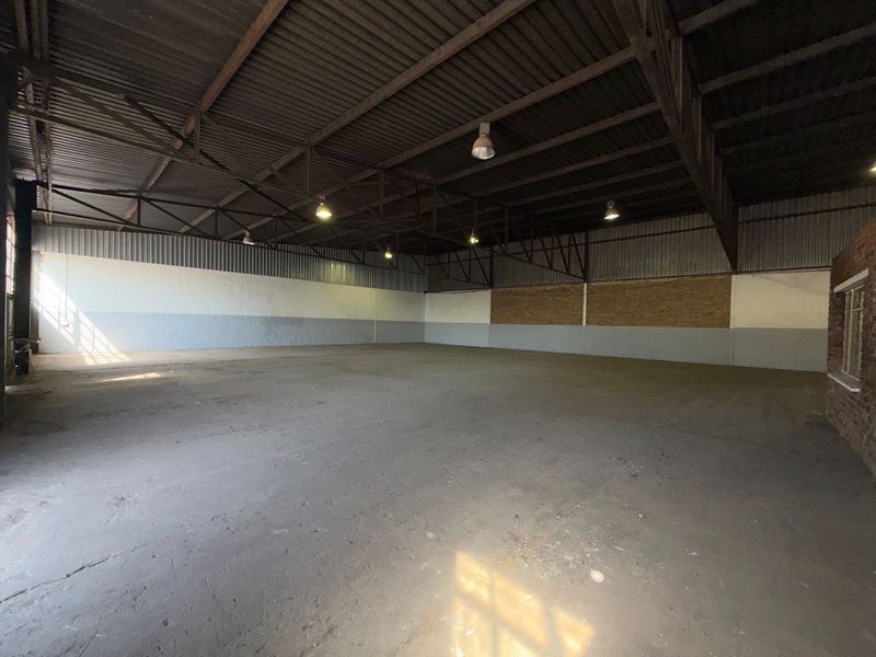 Spacious industrial warehouse unit featuring high exposed steel roof trusses, concrete flooring, and functional industrial lighting, suitable for various commercial or storage applications.