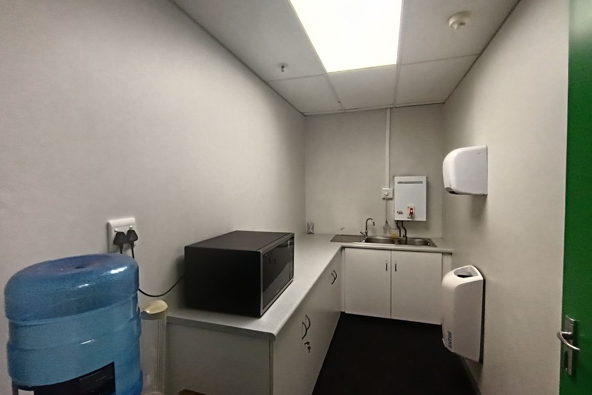 A functional office kitchenette featuring built-in cabinetry, a stainless steel sink, and an instant water heater, providing essential utility for staff.