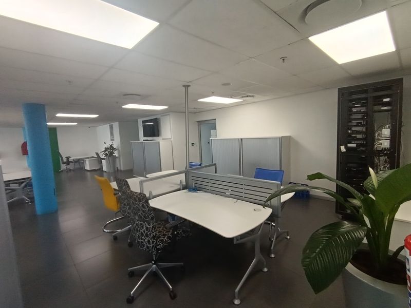 Open-plan office space featuring tiled flooring, recessed lighting, a dedicated server rack, and a central structural column.