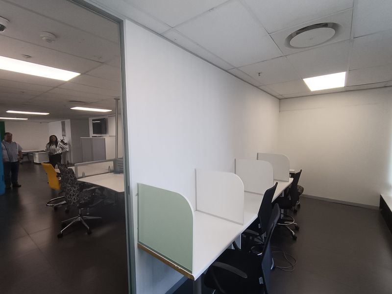 A functional office space featuring built-in desk partitions, a glass divider, and recessed lighting within a suspended ceiling system.