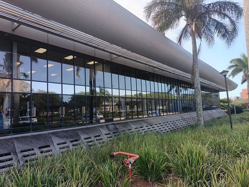 Exterior view of a modern office building featuring extensive glass curtain walling, a sleek metal roof canopy, and integrated concrete ventilation panels.