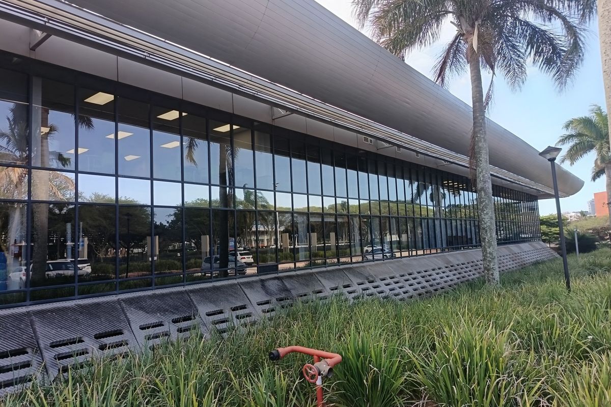 Exterior view of a modern office building featuring extensive glass curtain walling, a sleek metal roof canopy, and integrated concrete ventilation panels.