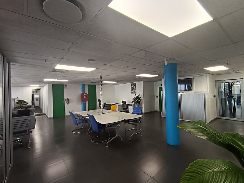Open-plan office space featuring tiled flooring, suspended ceilings with recessed lighting, and structural columns, providing a functional and professional work environment.
