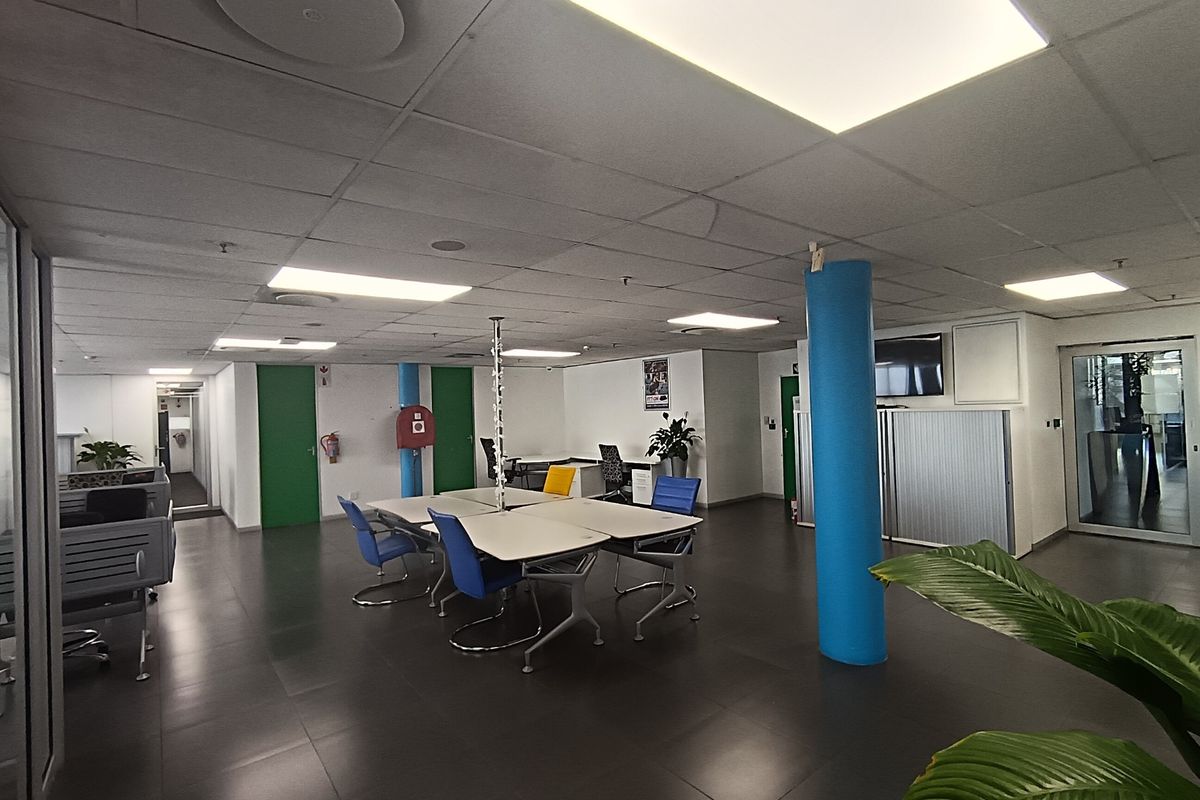 Open-plan office space featuring tiled flooring, suspended ceilings with recessed lighting, and structural columns, providing a functional and professional work environment.