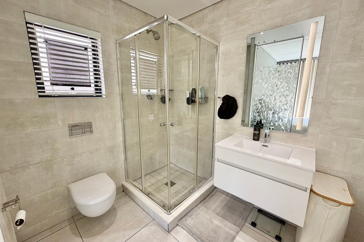 Modern bathroom featuring a wall-mounted toilet, glass shower enclosure, and a sleek vanity with an integrated basin and mirror.