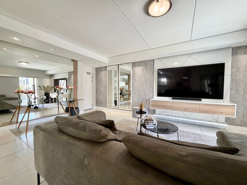Modern living room featuring a sleek built-in media console, large mirrored wall panels, recessed lighting, and neutral tiled flooring.