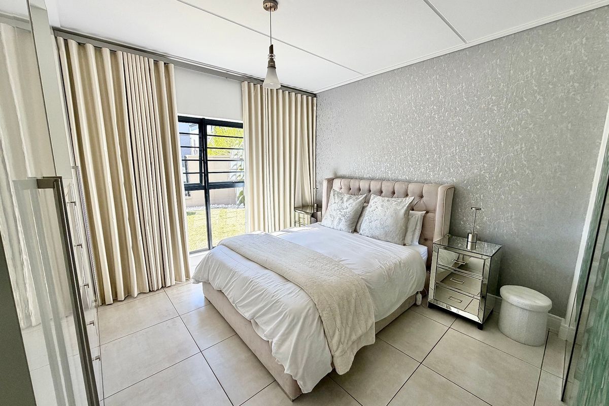 A well-maintained bedroom featuring large format floor tiles, textured feature wallpaper, and a sliding glass door providing access to the exterior.
