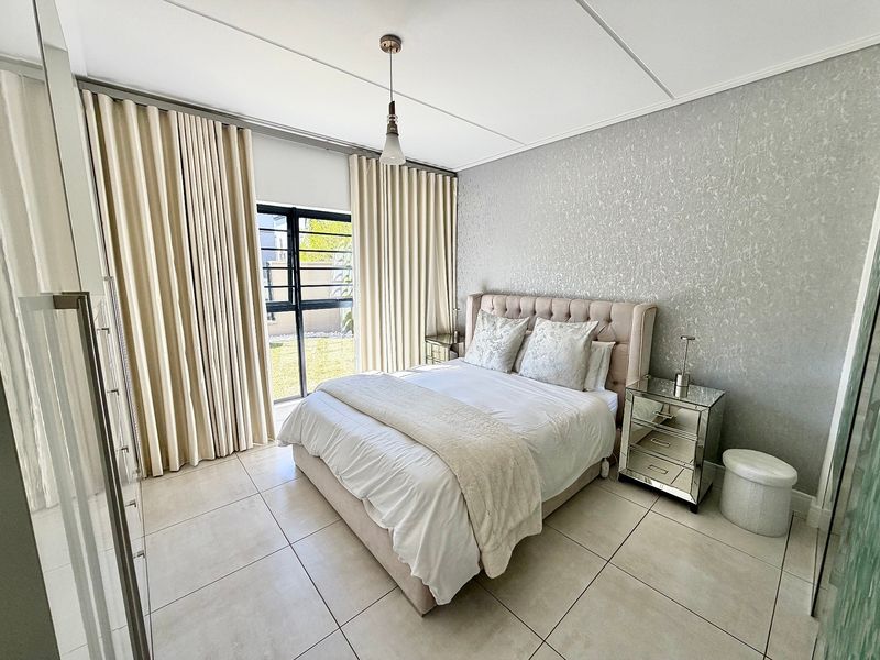 A well-maintained bedroom featuring large format floor tiles, textured feature wallpaper, and a sliding glass door providing access to the exterior.