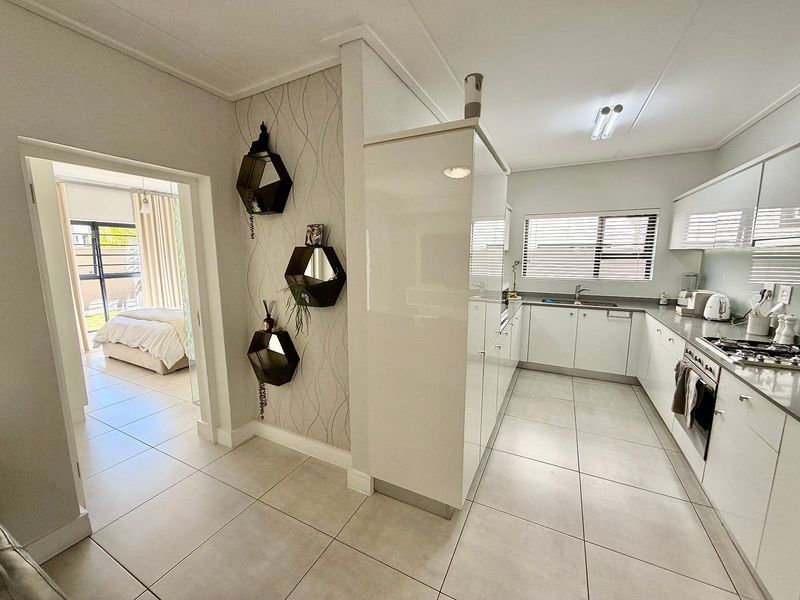 Modern kitchen featuring sleek white cabinetry, gas hob, built-in oven, and tiled flooring, with an open transition to the adjacent bedroom.