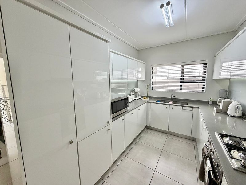 Modern kitchen featuring high-gloss white cabinetry, stone countertops, integrated appliances, and tiled flooring with ample natural light.
