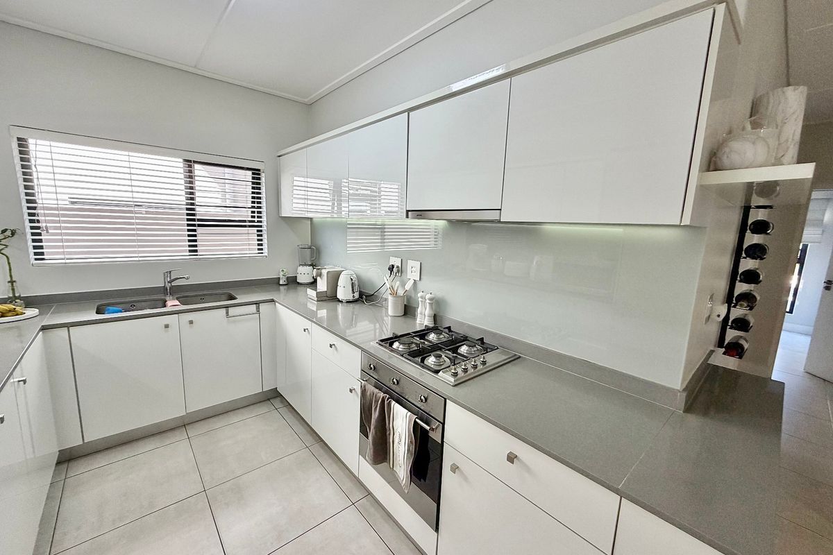 Modern kitchen featuring sleek white cabinetry, stone countertops, integrated stainless steel appliances, and a glass splashback with tiled flooring.