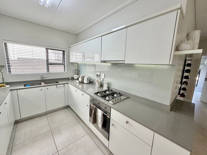 Modern kitchen featuring sleek white cabinetry, stone countertops, integrated stainless steel appliances, and a glass splashback with tiled flooring.