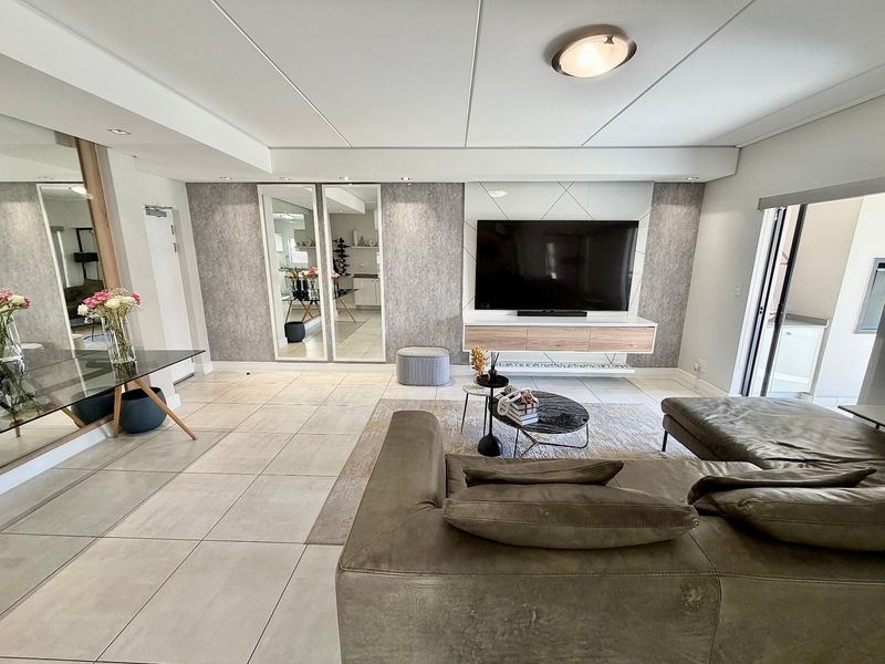 Modern living room featuring large format floor tiles, a custom built-in media console, and decorative mirrored wall panels with integrated lighting.