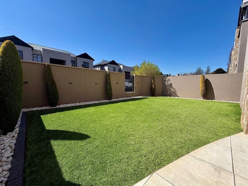 A well-maintained private garden featuring artificial lawn, paved patio area, and high boundary walls with integrated lighting.
