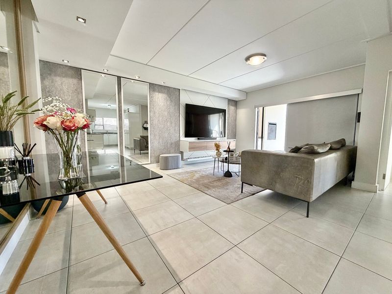 Modern open-plan living area featuring large format floor tiles, recessed lighting, and a sleek built-in media wall with mirrored accents.