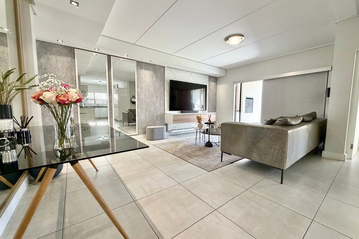 Modern open-plan living area featuring large format floor tiles, recessed lighting, and a sleek built-in media wall with mirrored accents.