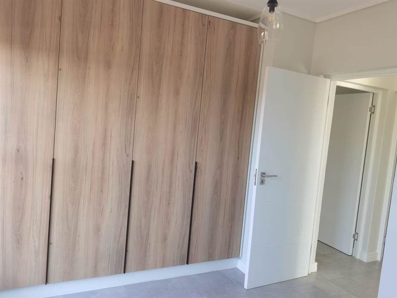 A clean, modern bedroom featuring light wood-grain built-in cupboards, neutral tiled flooring, and a crisp white interior door.