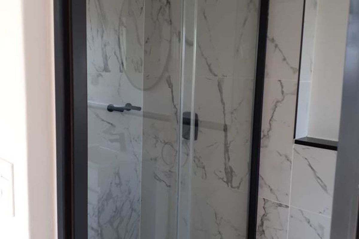 Modern bathroom featuring a sleek glass shower enclosure with black framing and elegant marble-look wall tiles.