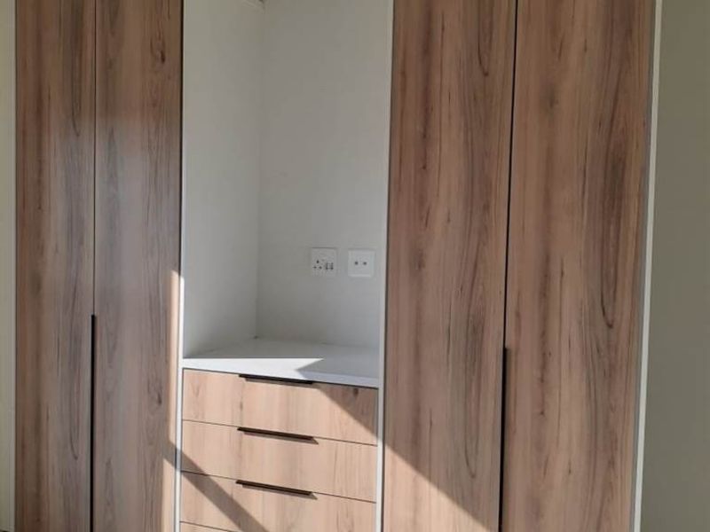 A modern bedroom featuring floor-to-ceiling built-in cupboards with wood-grain finish and an integrated vanity or desk area with drawers.