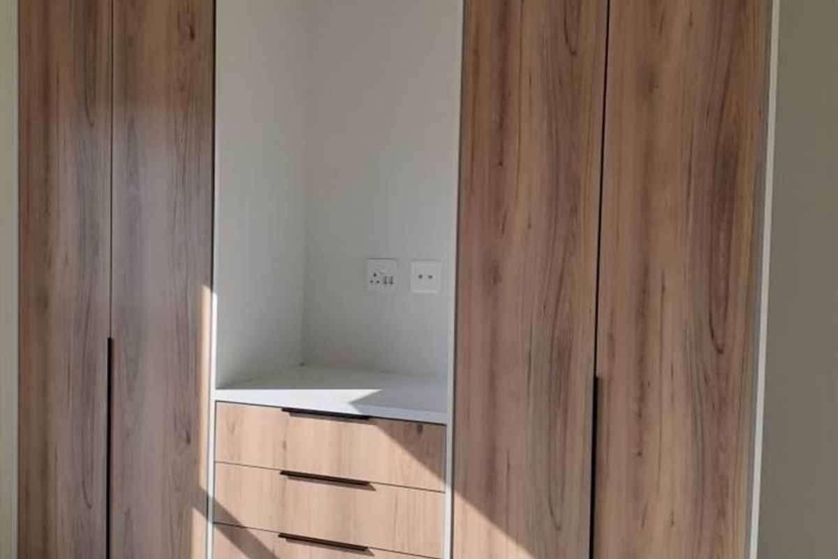 A modern bedroom featuring floor-to-ceiling built-in cupboards with wood-grain finish and an integrated vanity or desk area with drawers.
