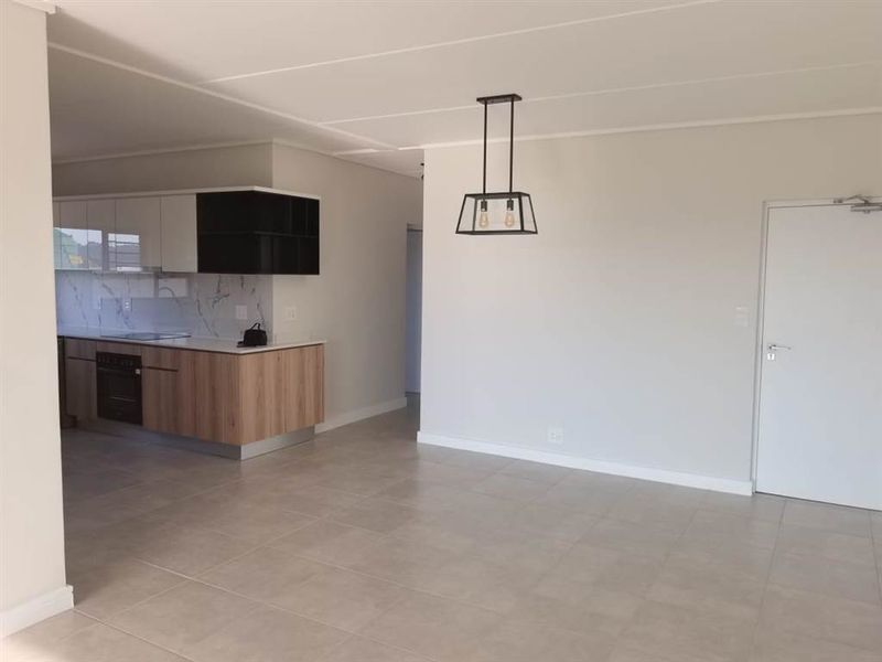 Modern open-plan living area featuring a sleek kitchen with built-in cabinetry, marble-look splashback, and neutral tiled flooring throughout.