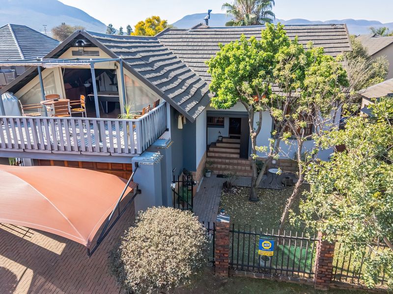 Aerial view of the front facade featuring a tiled roof, elevated balcony, paved driveway with shade sail, and secure perimeter fencing.
