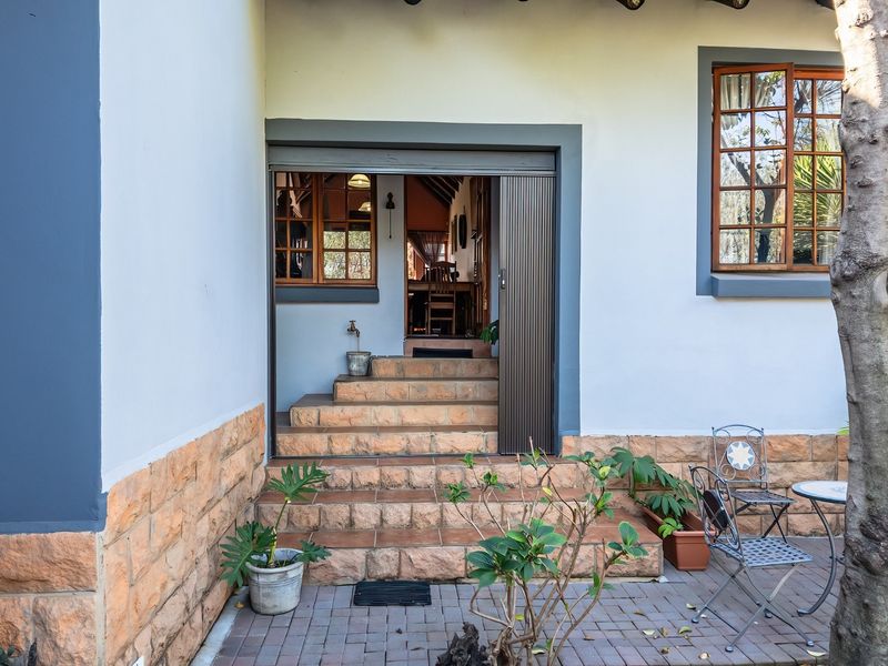 Rear entrance featuring tiled steps, stone cladding, and a sliding security gate, providing access to the interior living space.